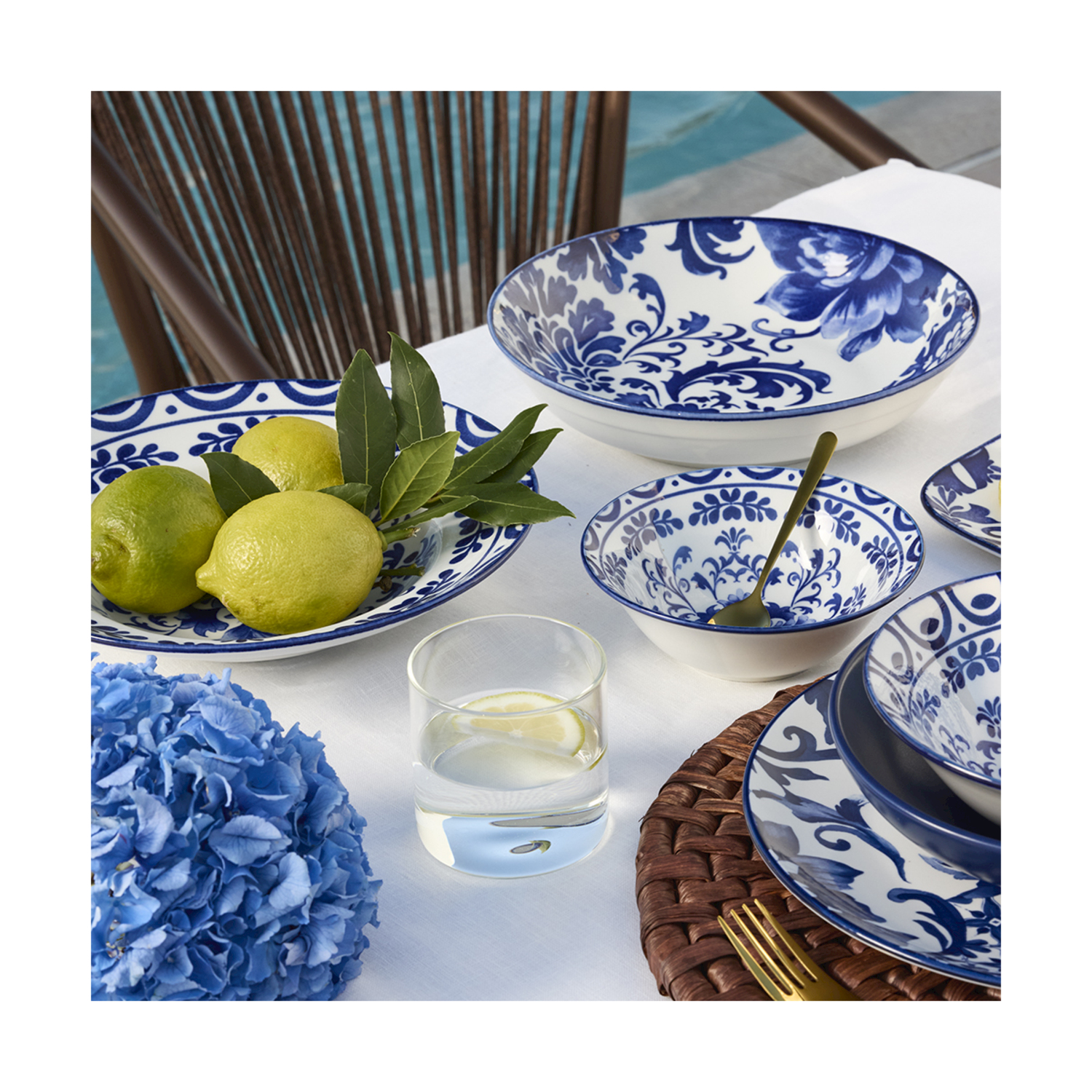 Piatti bianco-blu fantasia con limoni, ortensia blu e un bicchiere d'acqua.