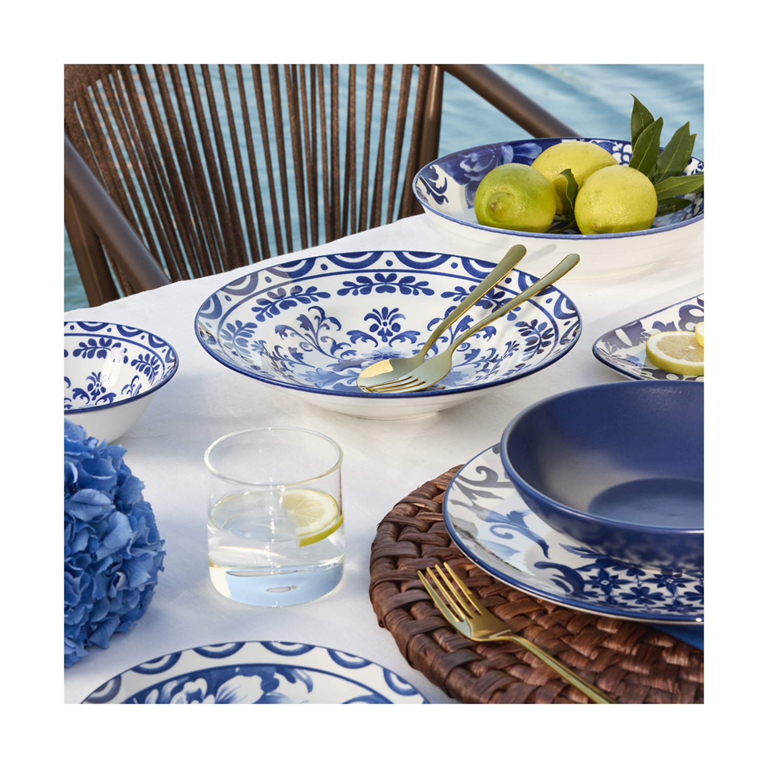 Una tavola apparecchiata con ceramiche blu e bianche, limoni e un bicchiere d'acqua all'aperto.