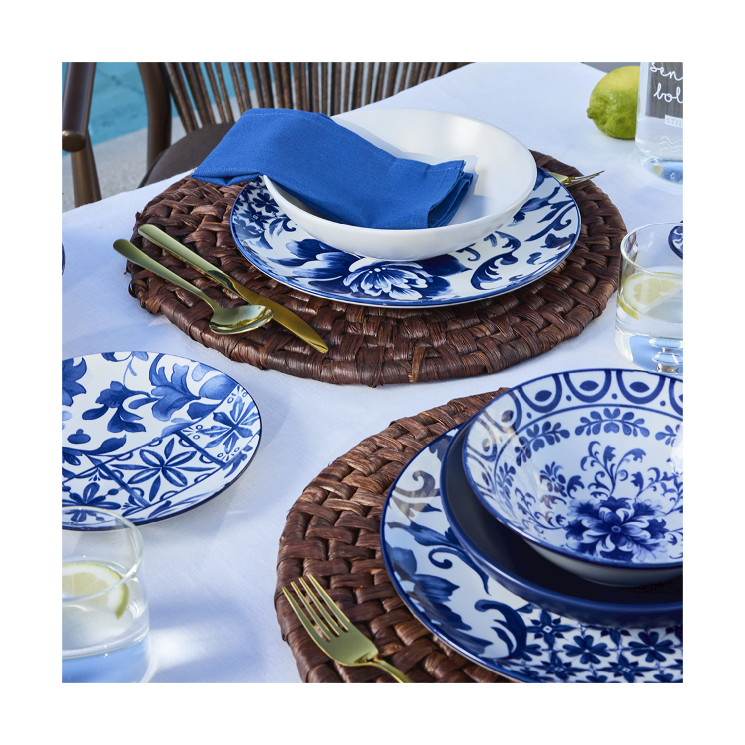 Tavola apparecchiata con stoviglie blu e bianche, posate dorate e bicchieri d'acqua.