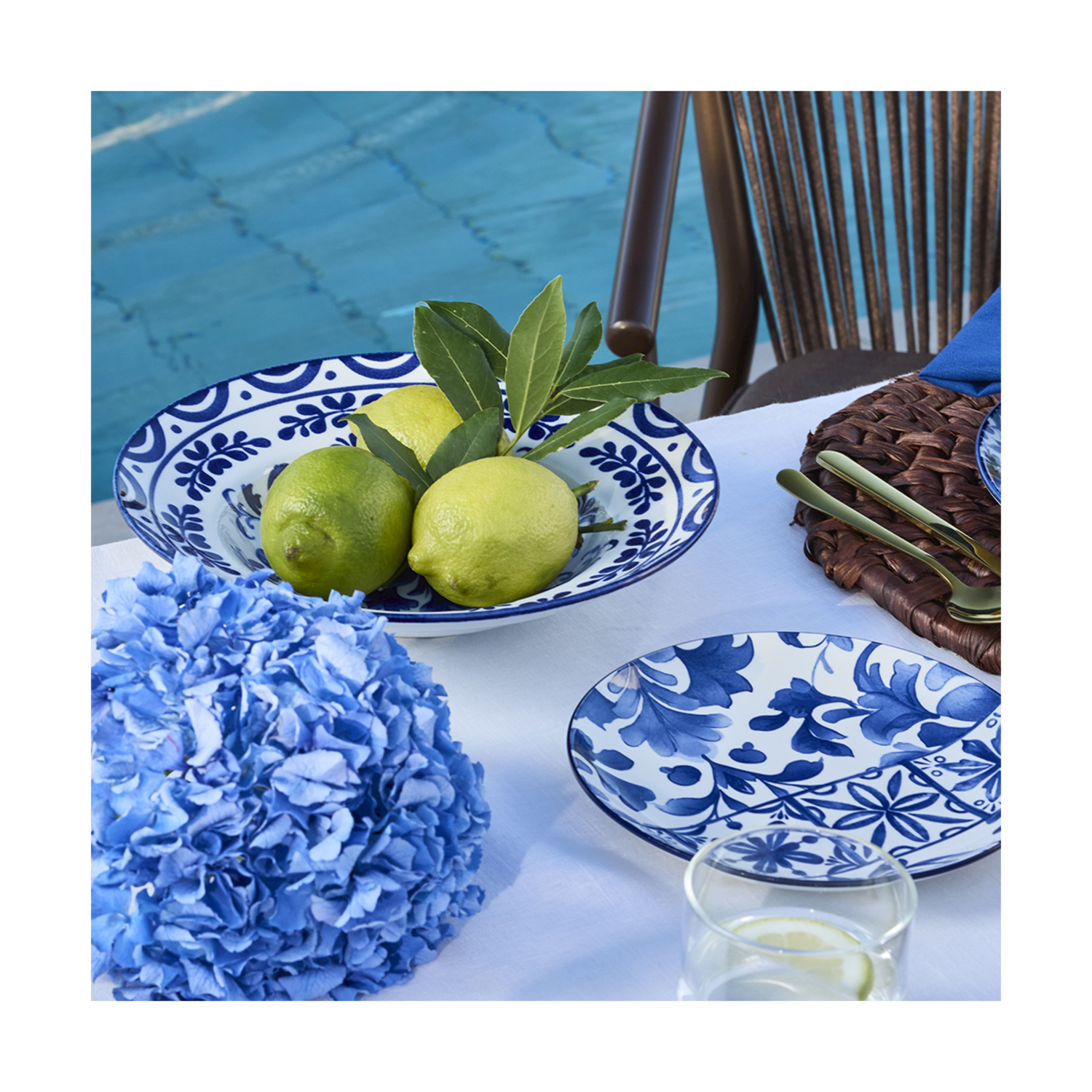 Ciotola fantasia blu e bianca con limoni, ortensia blu e piatto vicino alla piscina.