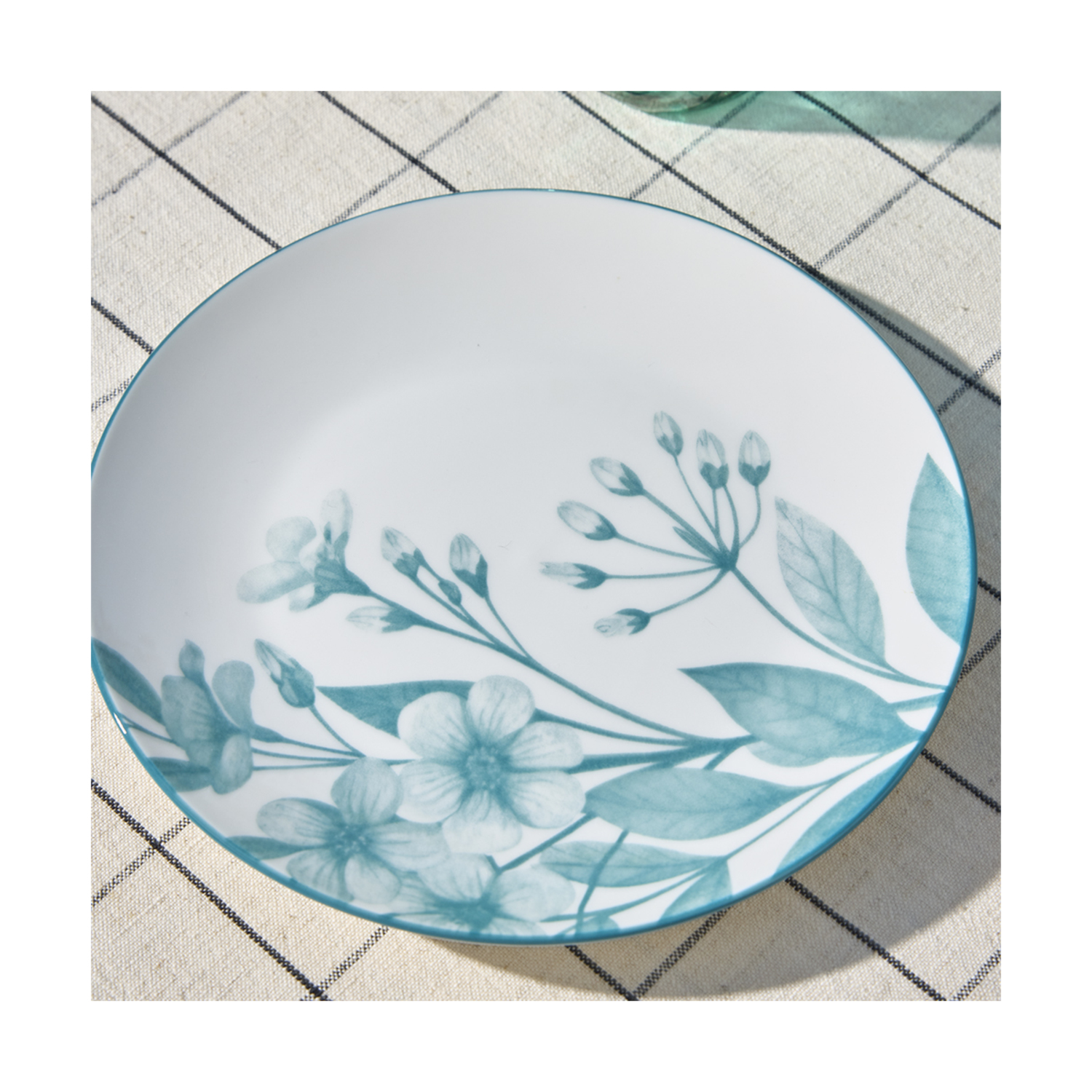 Piatto in ceramica bianca con motivo floreale blu, su tovaglia a quadri.