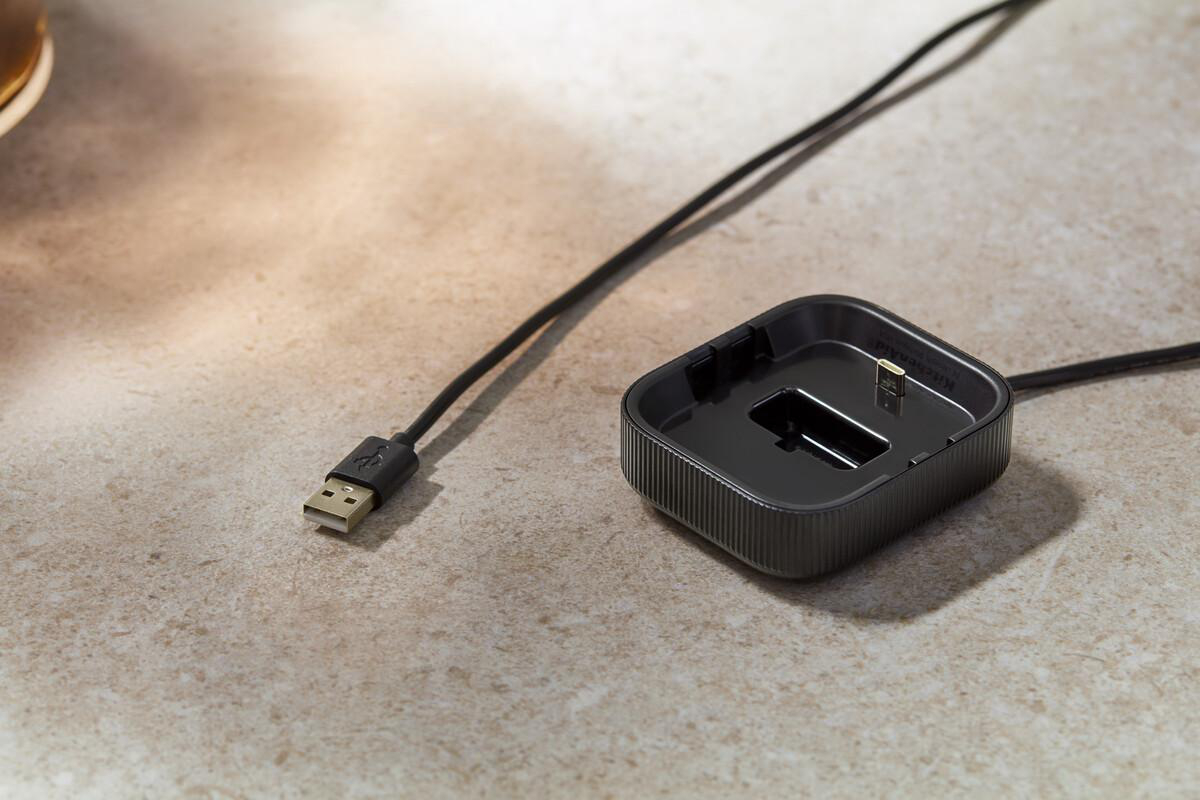 Ein schwarzes USB-Kabel liegt neben einer schwarzen Ladestation auf einer Steinplatte.