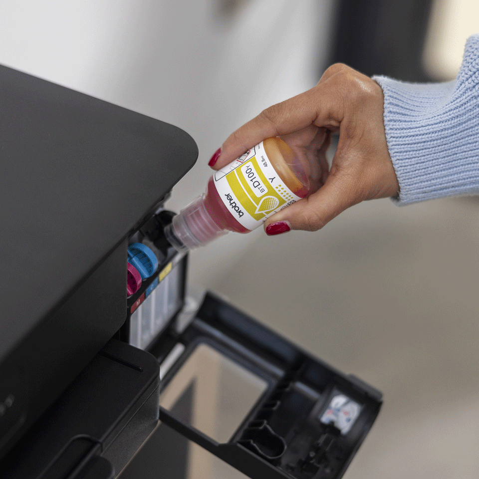 Ręka wlewa żółty tusz z butelki do drukarki.