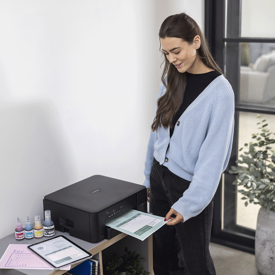 Kobieta w niebieskim kardiganie drukuje dokument z czarnej drukarki Brother.