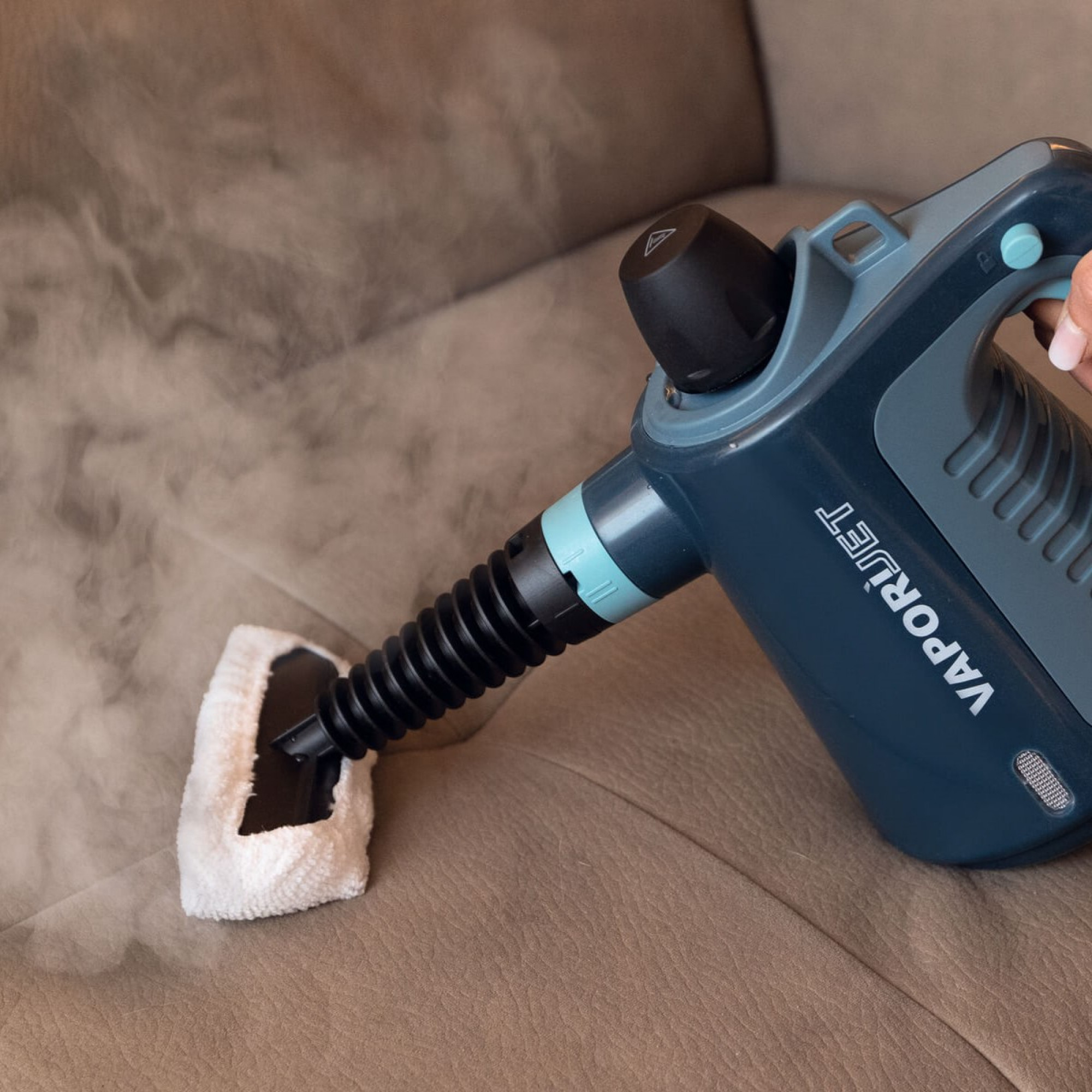 Un limpiador a vapor limpia un sofá marrón con un paño blanco y vapor.