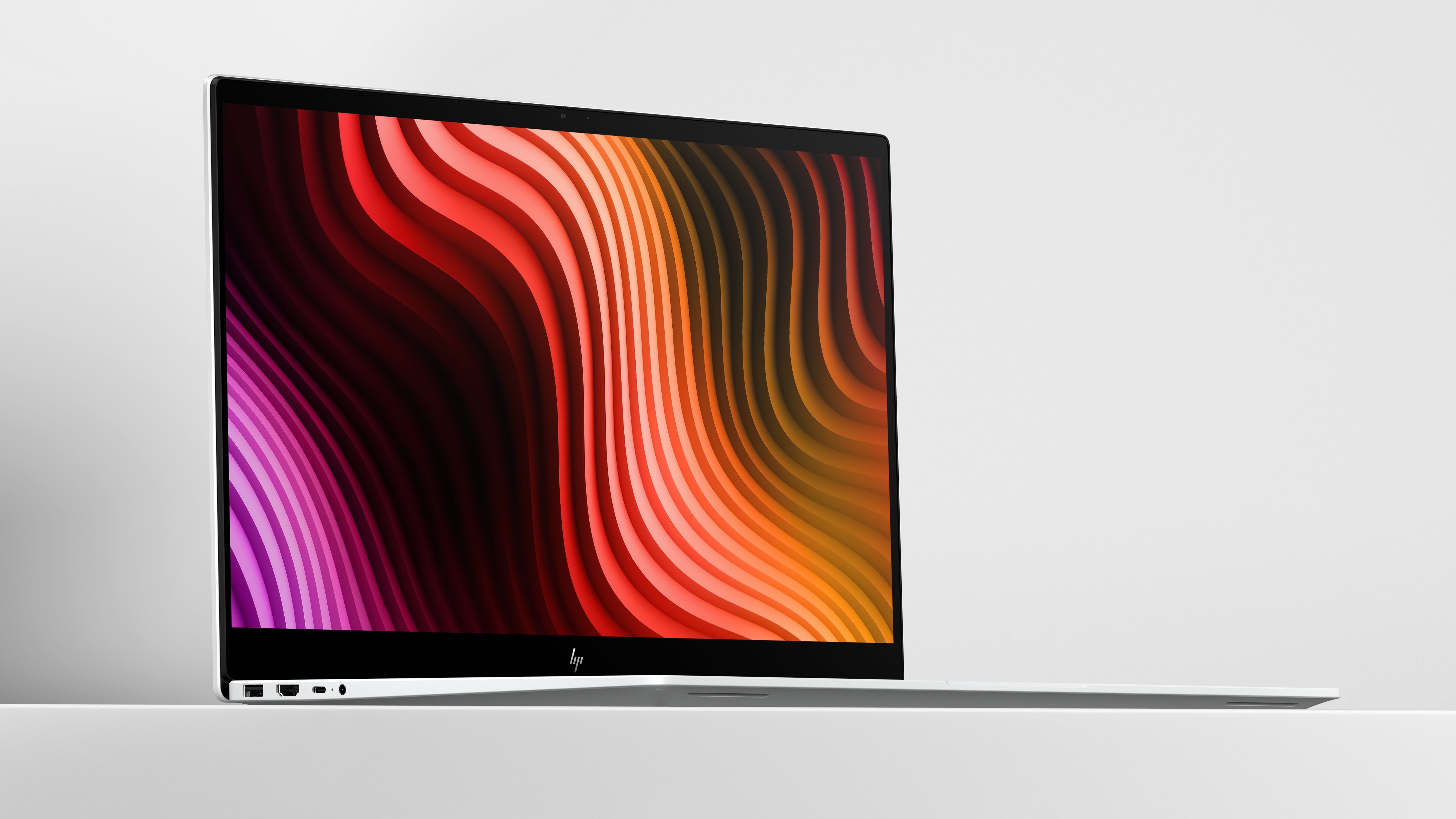 Srebrny laptop wyświetlający kolorowe, faliste tło na ekranie.