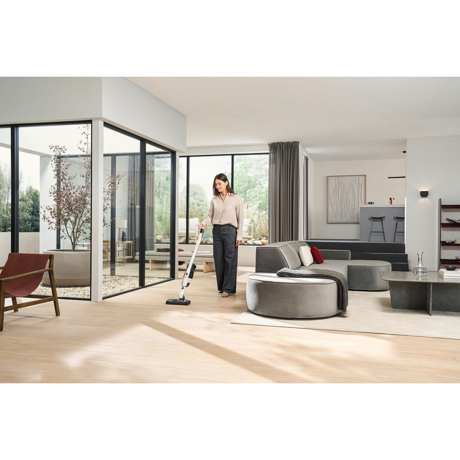 Une femme passe l'aspirateur dans un salon moderne avec un aspirateur blanc.