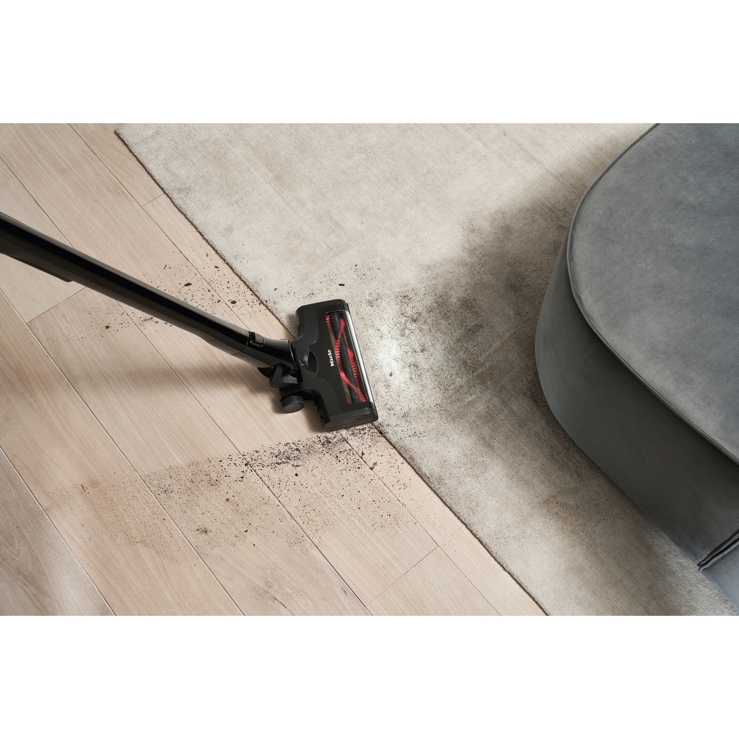 A black vacuum cleaner cleans dirt from wood and carpet.