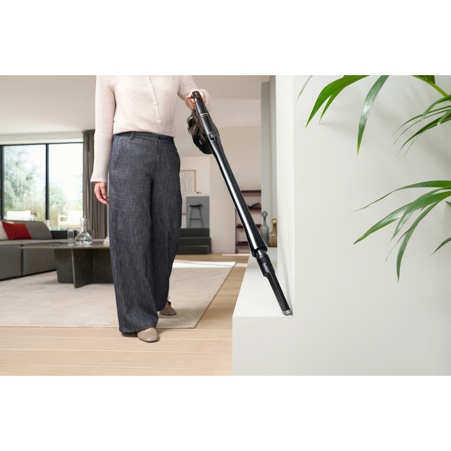 A person vacuums a white baseboard with a black handheld vacuum cleaner.