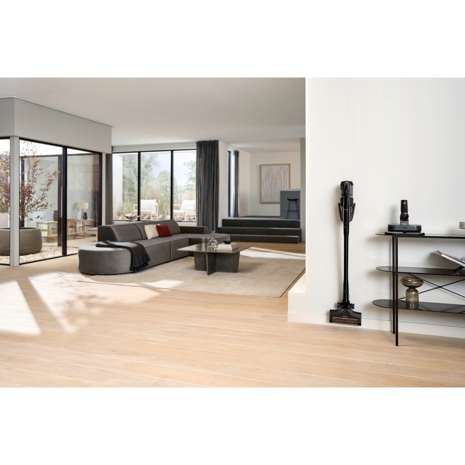 Un salon moderne avec un canapé gris, une table basse et un aspirateur sans fil.