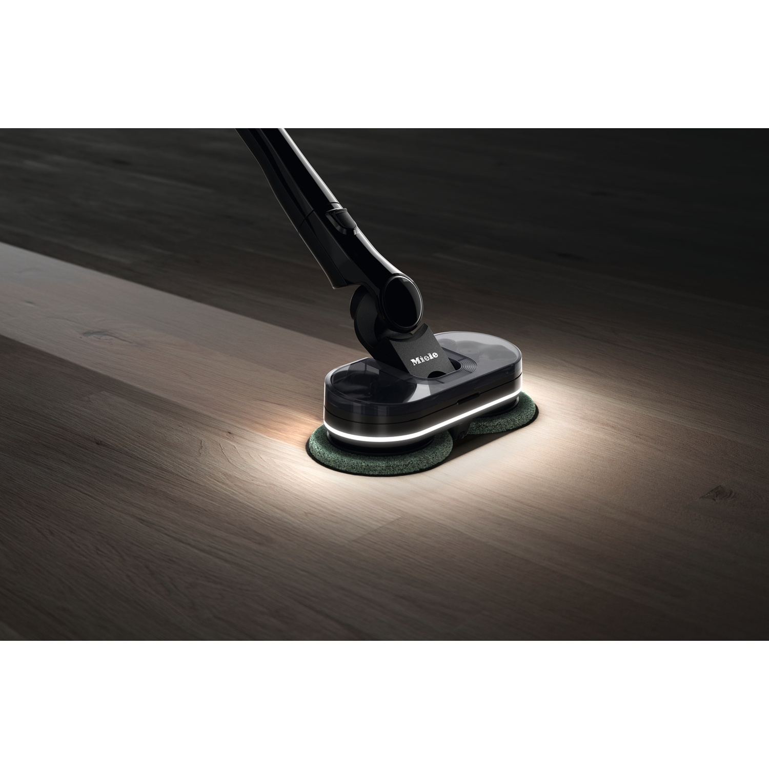 Un lave-sol Miele noir avec tampons verts sur un parquet.