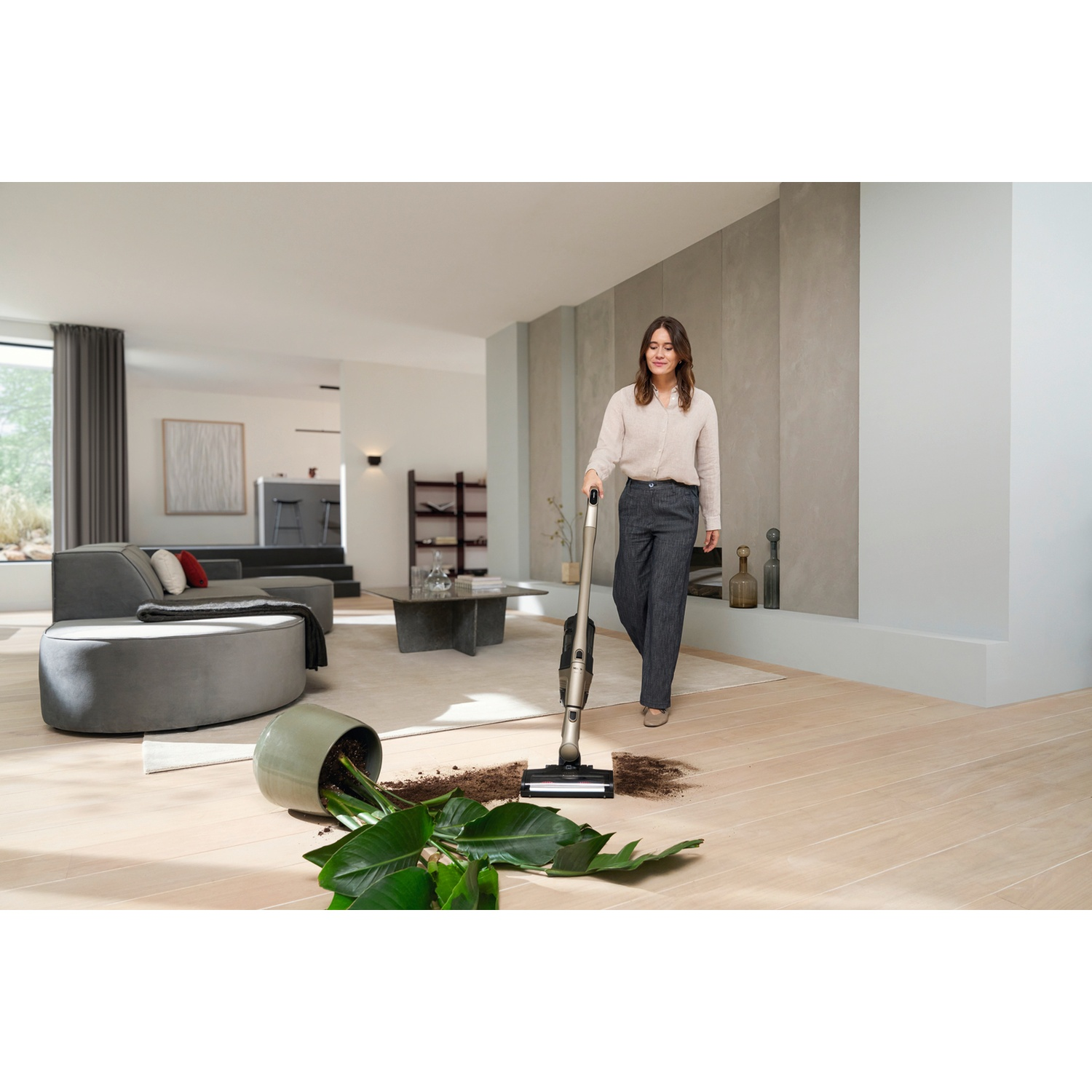 Une femme passe l'aspirateur sur une plante renversée dans un salon moderne.