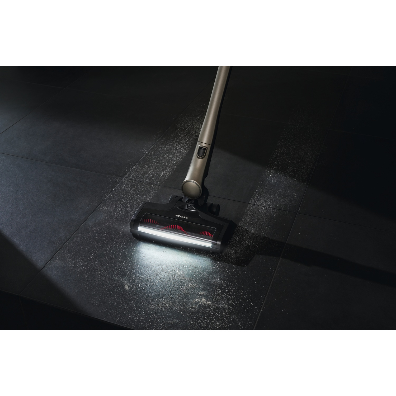 Un aspirateur sans fil nettoie la poussière d'un sol carrelé sombre.