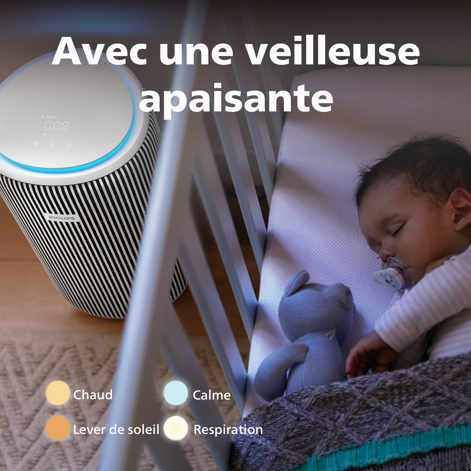 Un bébé dort dans un lit à côté d'un purificateur d'air et d'un ours en peluche.