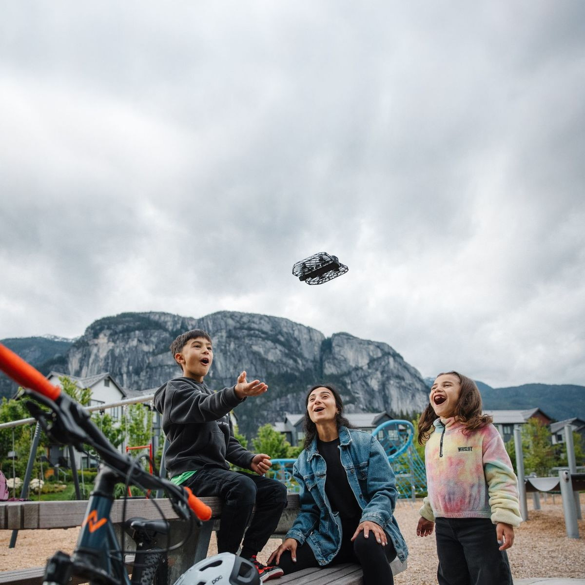 Famiglia guarda un drone volare all'aperto con montagne sullo sfondo.