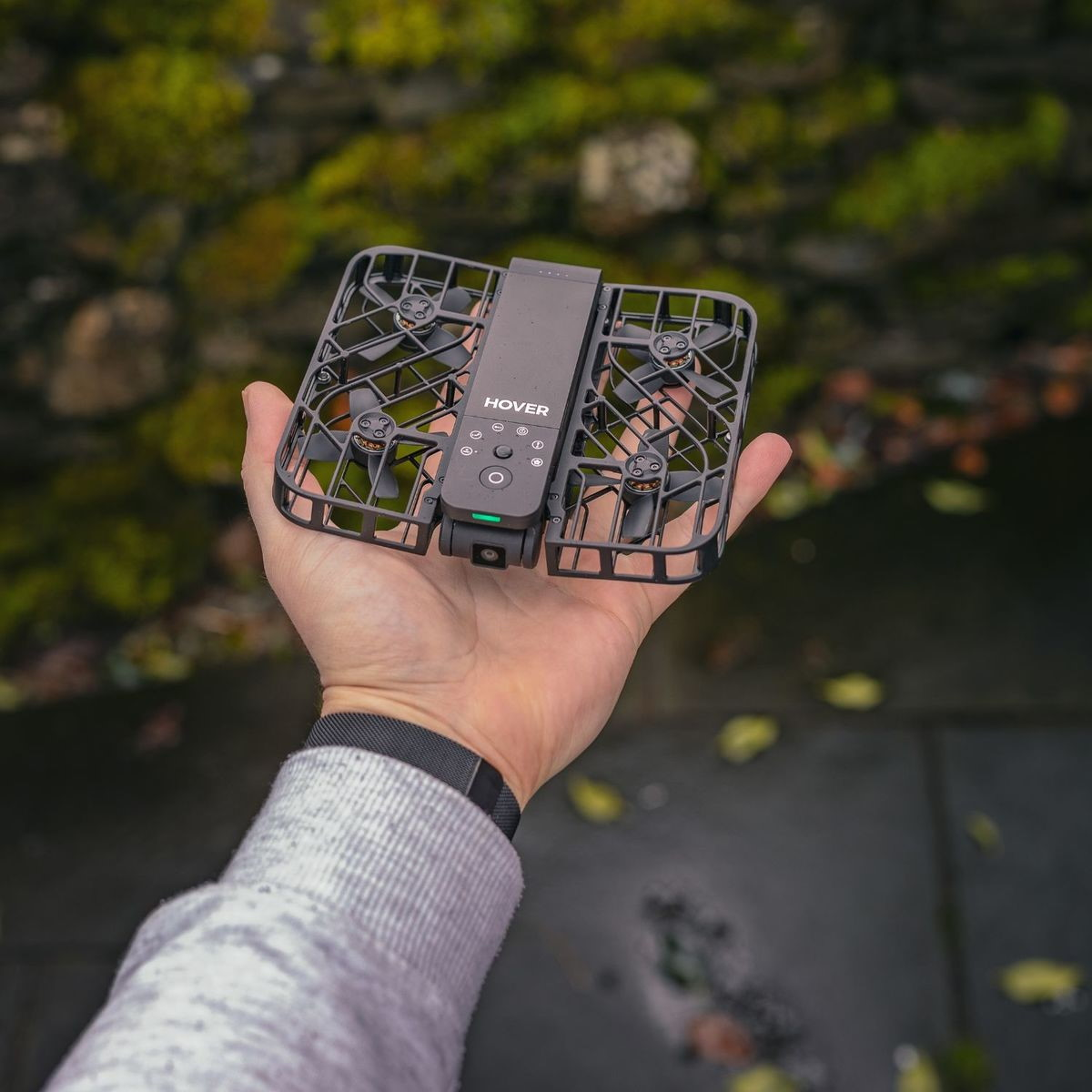 Una mano tiene un piccolo drone nero con eliche e pulsanti.