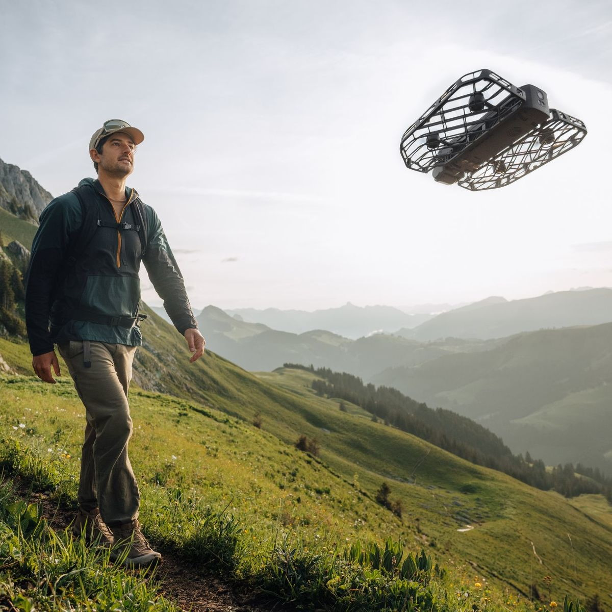 Un uomo cammina su un sentiero di montagna, un drone vola nel cielo.