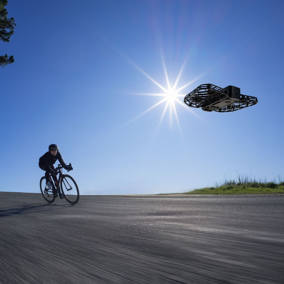 Un ciclista pedala su una strada sotto un cielo blu brillante mentre un drone vola.