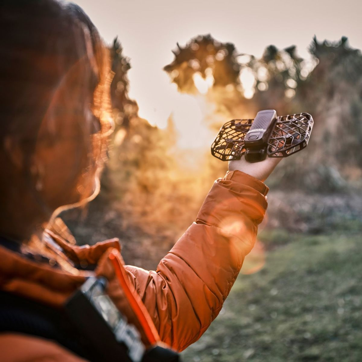 Una persona tiene un drone in mano con il sole che sorge sullo sfondo.