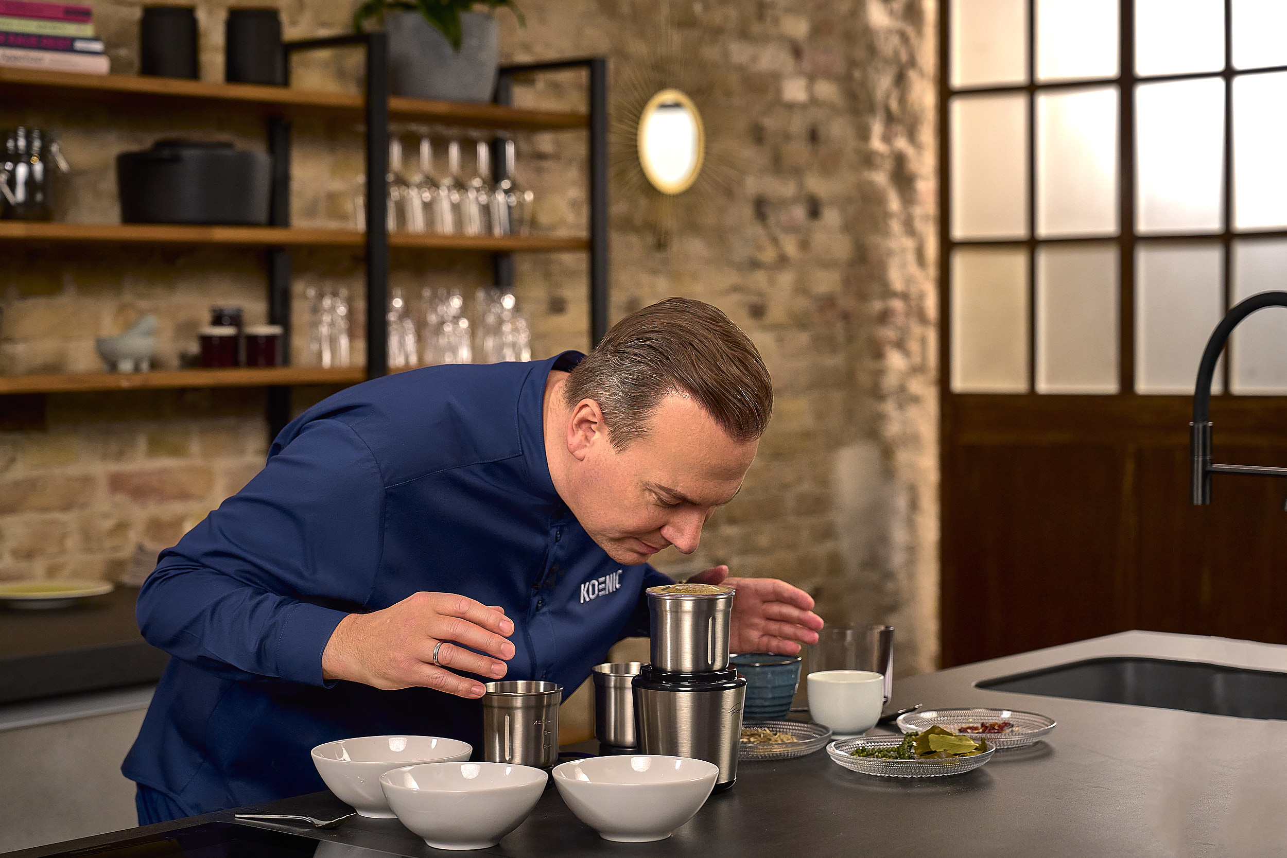 Ein Mann in einem blauen Hemd beugt sich über einen Mixer und riecht daran.