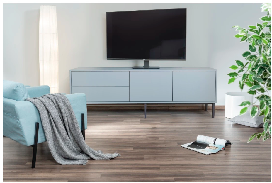 Jasnoniebieska sofa z szarym pledem, szafka RTV, telewizor i lampa.