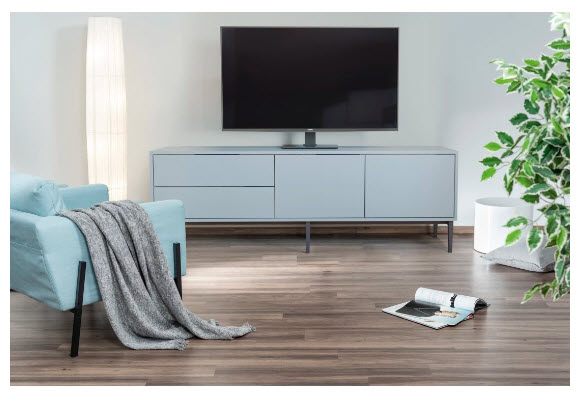 Jasnoniebieska sofa z kocem, szafka RTV z telewizorem, lampa stojąca i roślina.