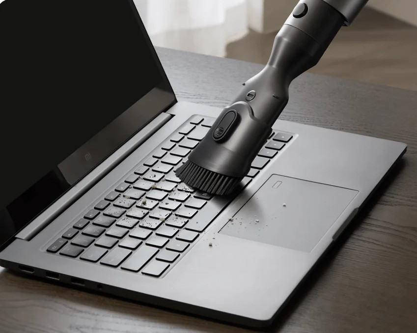 Odkurzacz czyści klawiaturę laptopa na drewnianym stole.