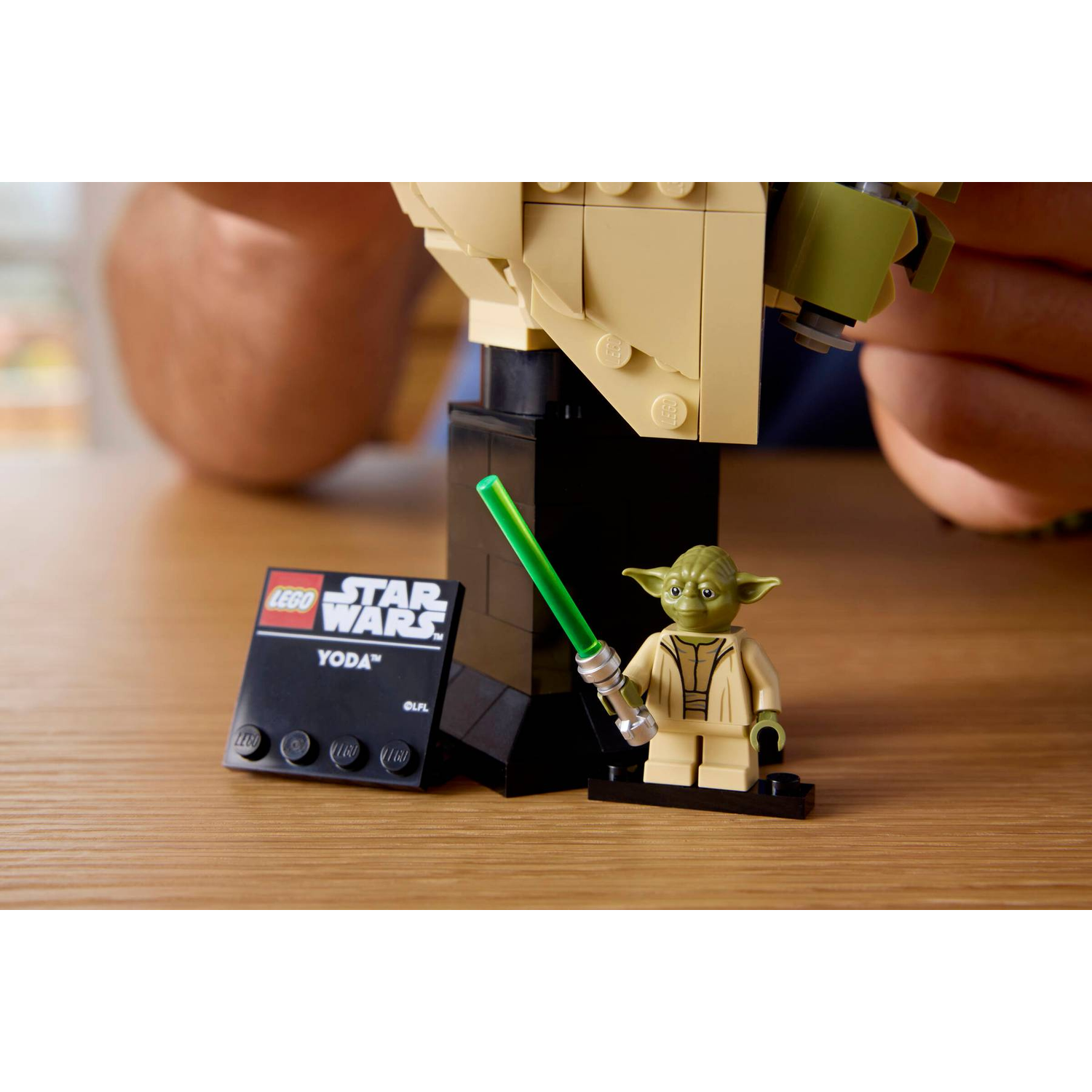 A Lego Yoda with a lightsaber stands next to an info plaque.