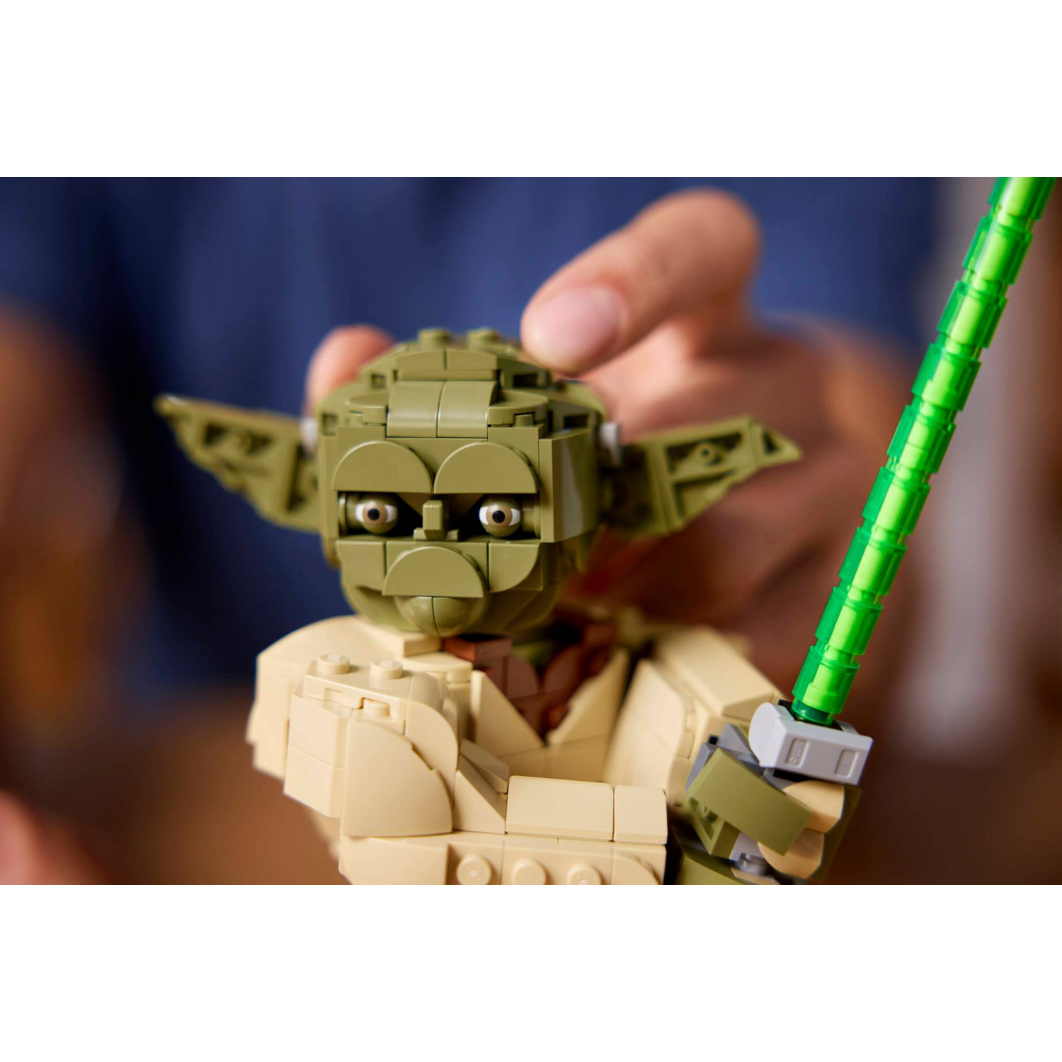 A Lego Yoda figure with a green lightsaber is held by hands.