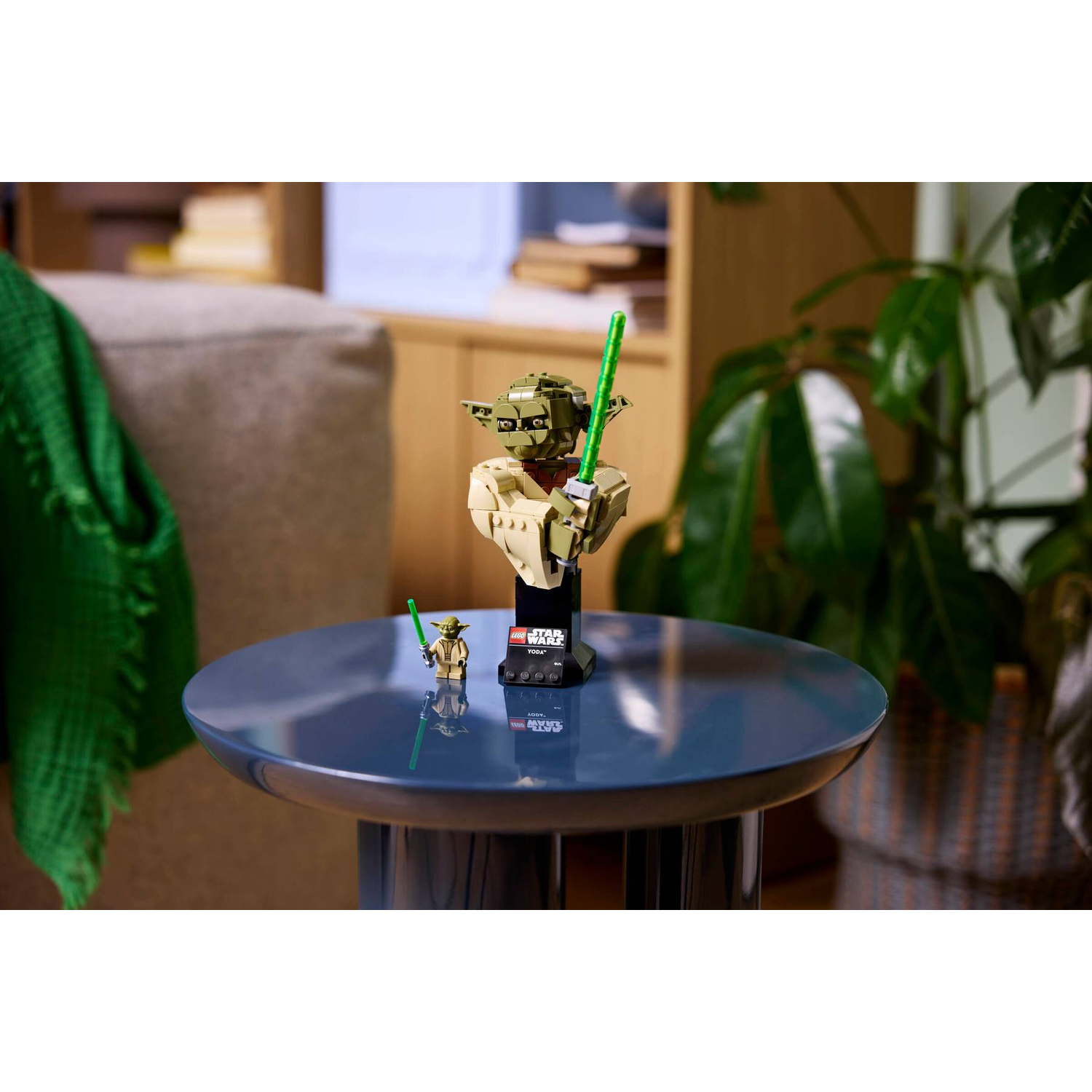 Lego bust of Yoda holding a green lightsaber on a blue table.