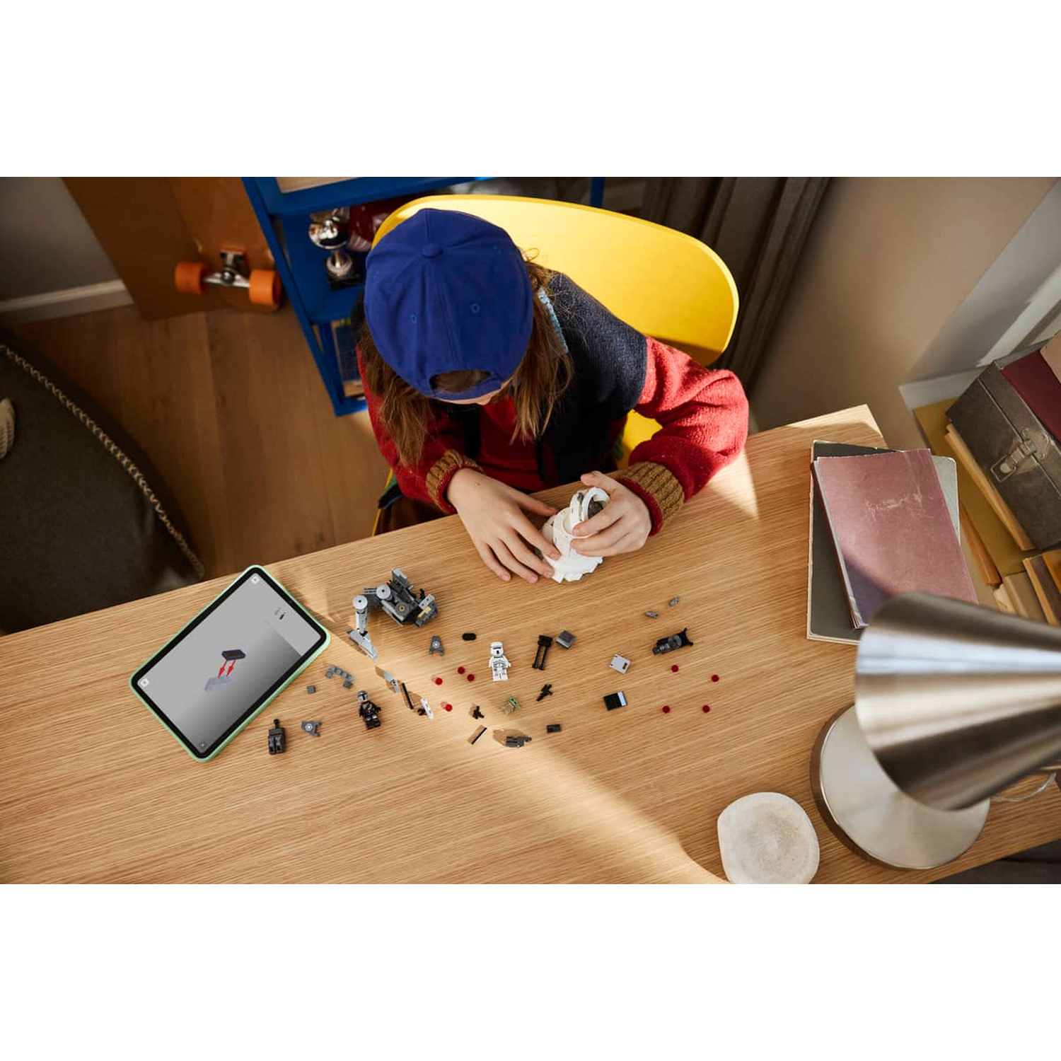 A child wearing a blue cap builds with LEGO on a wooden table.