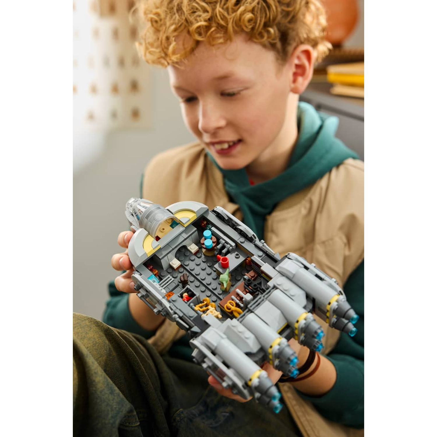 A boy with curly hair holds a detailed gray Lego spaceship.
