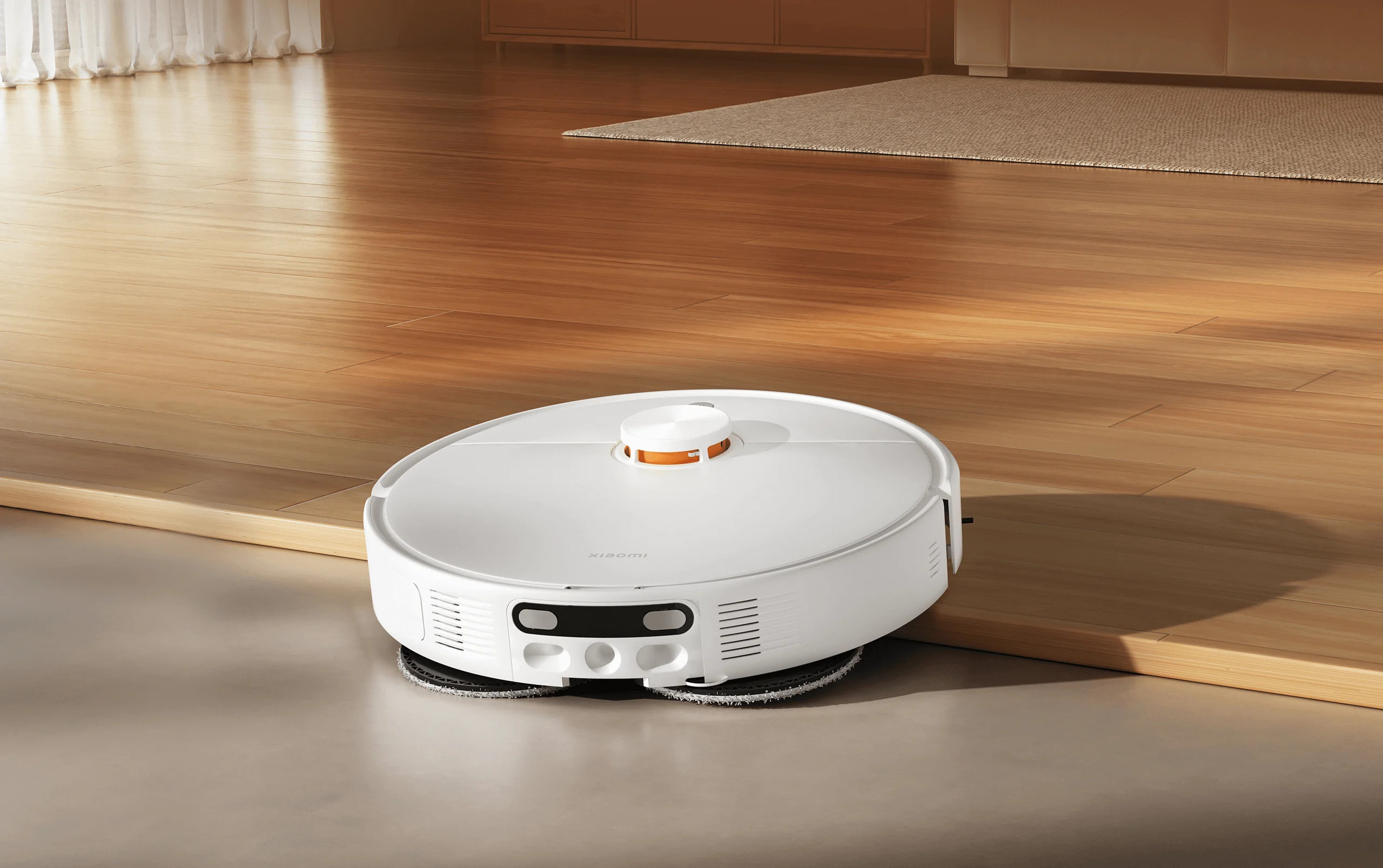 Biały robot sprzątający Xiaomi z pomarańczowymi akcentami czyści drewnianą podłogę.