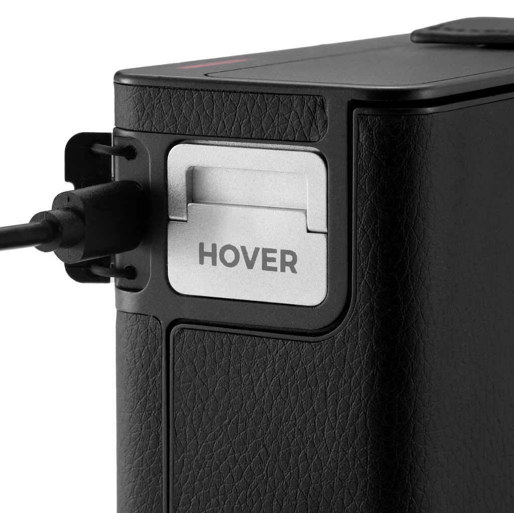 Appareil noir avec bouton argenté HOVER et câble. Surface texturée.