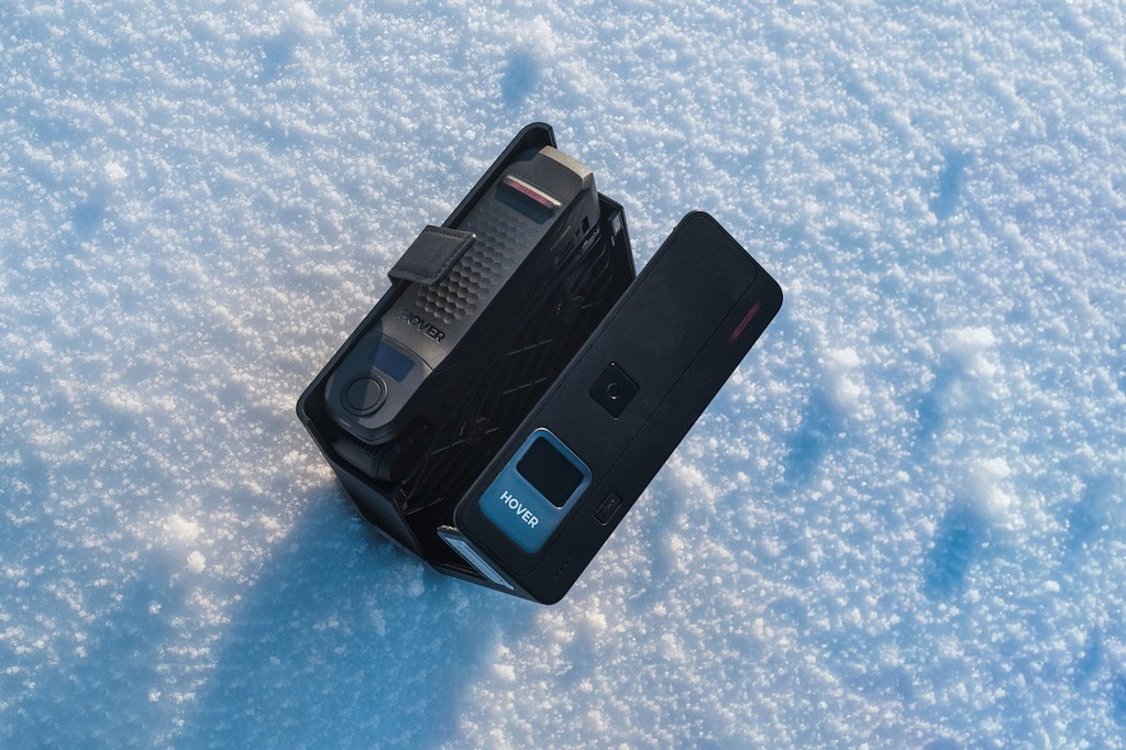 Deux appareils noirs Hover sur la neige, un dans son étui.