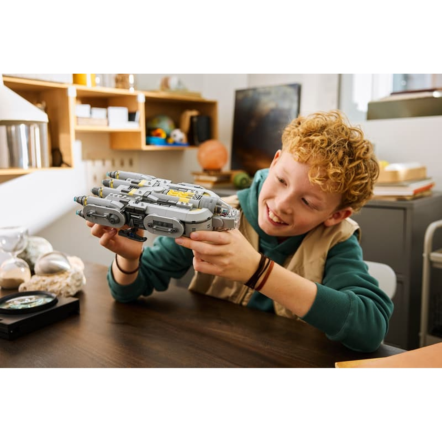 A boy with curly hair holds a gray spaceship toy.