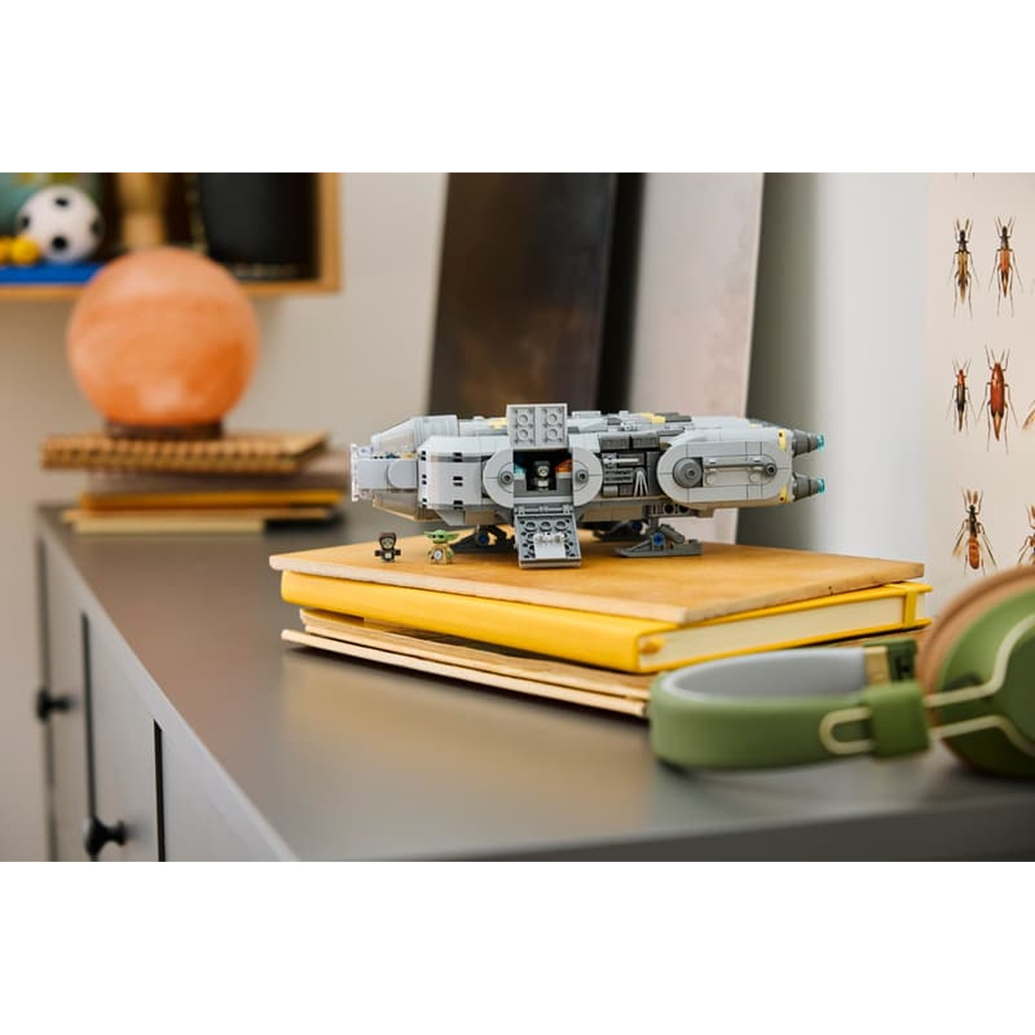 Gray spaceship model on yellow books, with figures and headphones nearby.