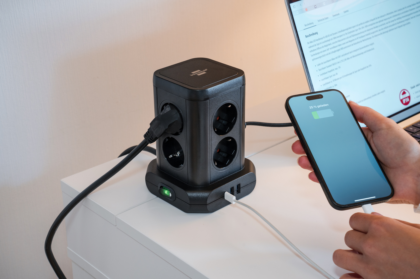 Schwarzer Mehrfachsteckdosenwürfel mit angeschlossenen Kabeln und einem Handy.