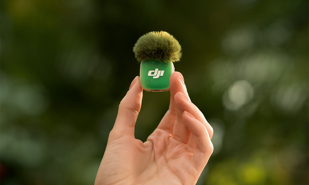 Dłoń trzyma mały, zielony mikrofon z futrem na górze. Widoczne logo DJI.