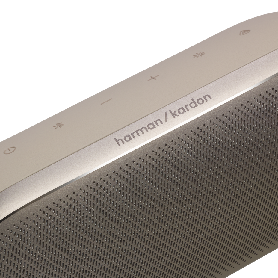 Harman/Kardon logolu ve düğmeli altın rengi hoparlör yakın çekimi.