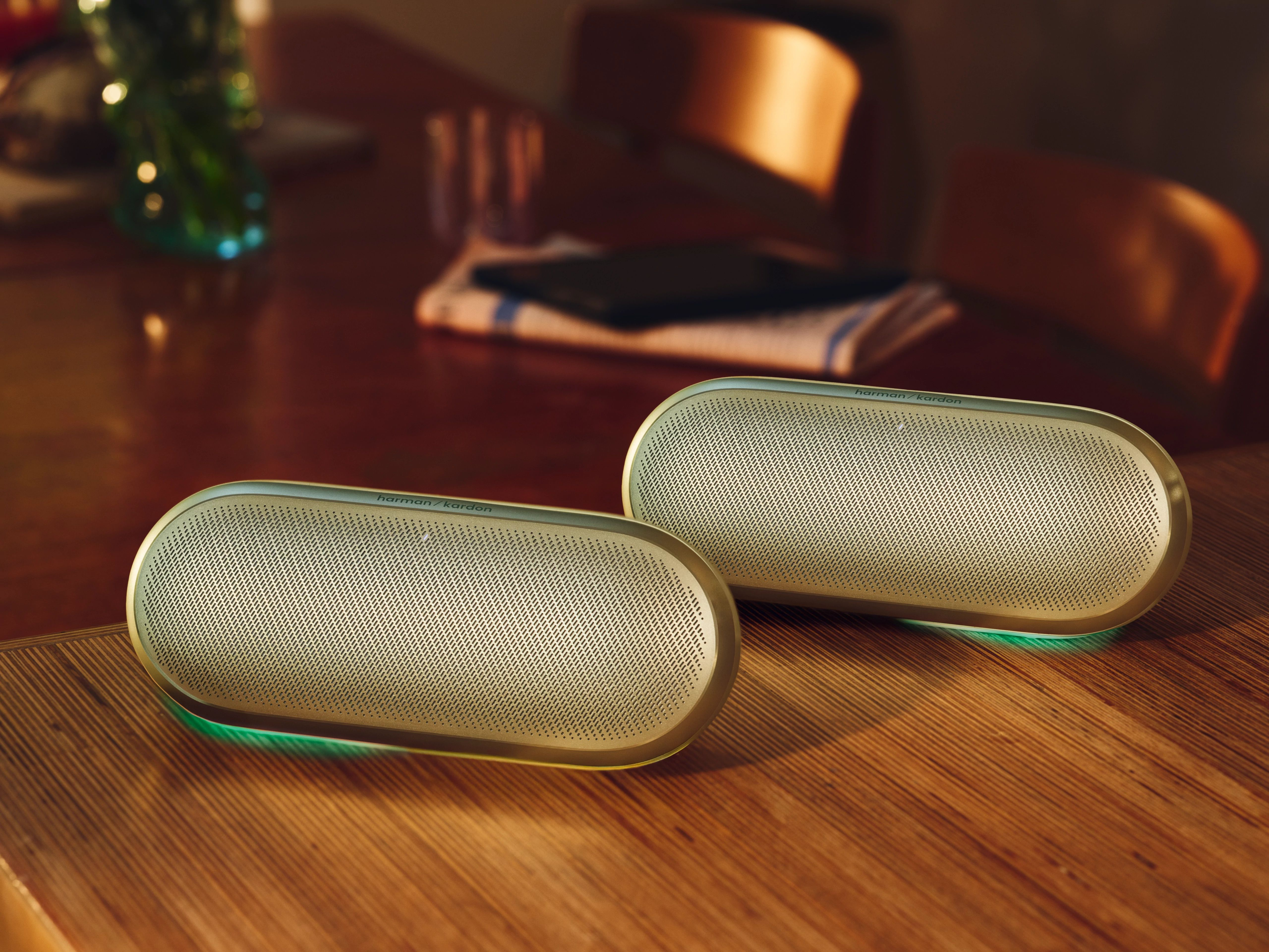 Ahşap masa üzerinde yeşil ışıklı iki altın Harman Kardon hoparlör.
