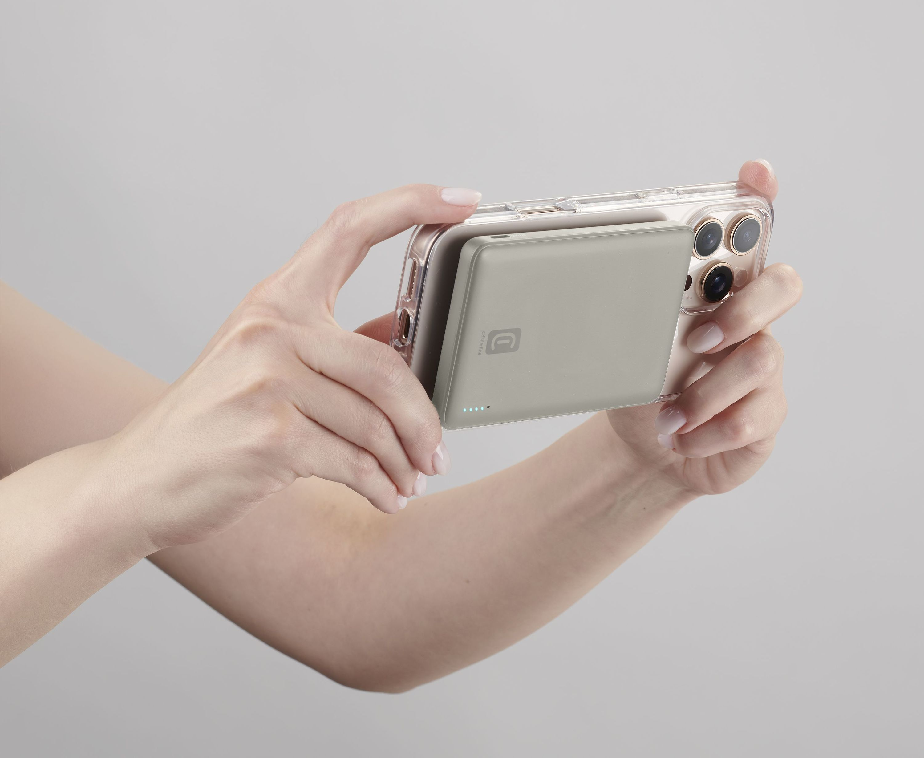 Eller gri arka plan önünde MagSafe şarj cihazı takılı bir iPhone tutuyor.