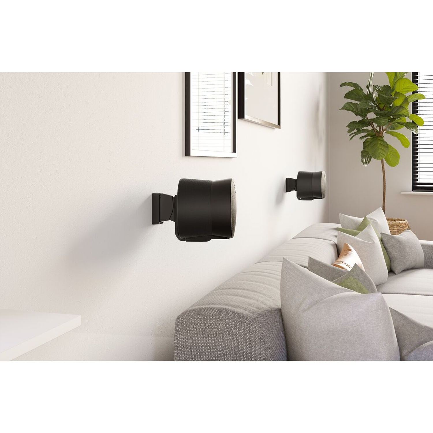 Haut-parleurs noirs sur un mur blanc au-dessus d'un canapé avec coussins gris.