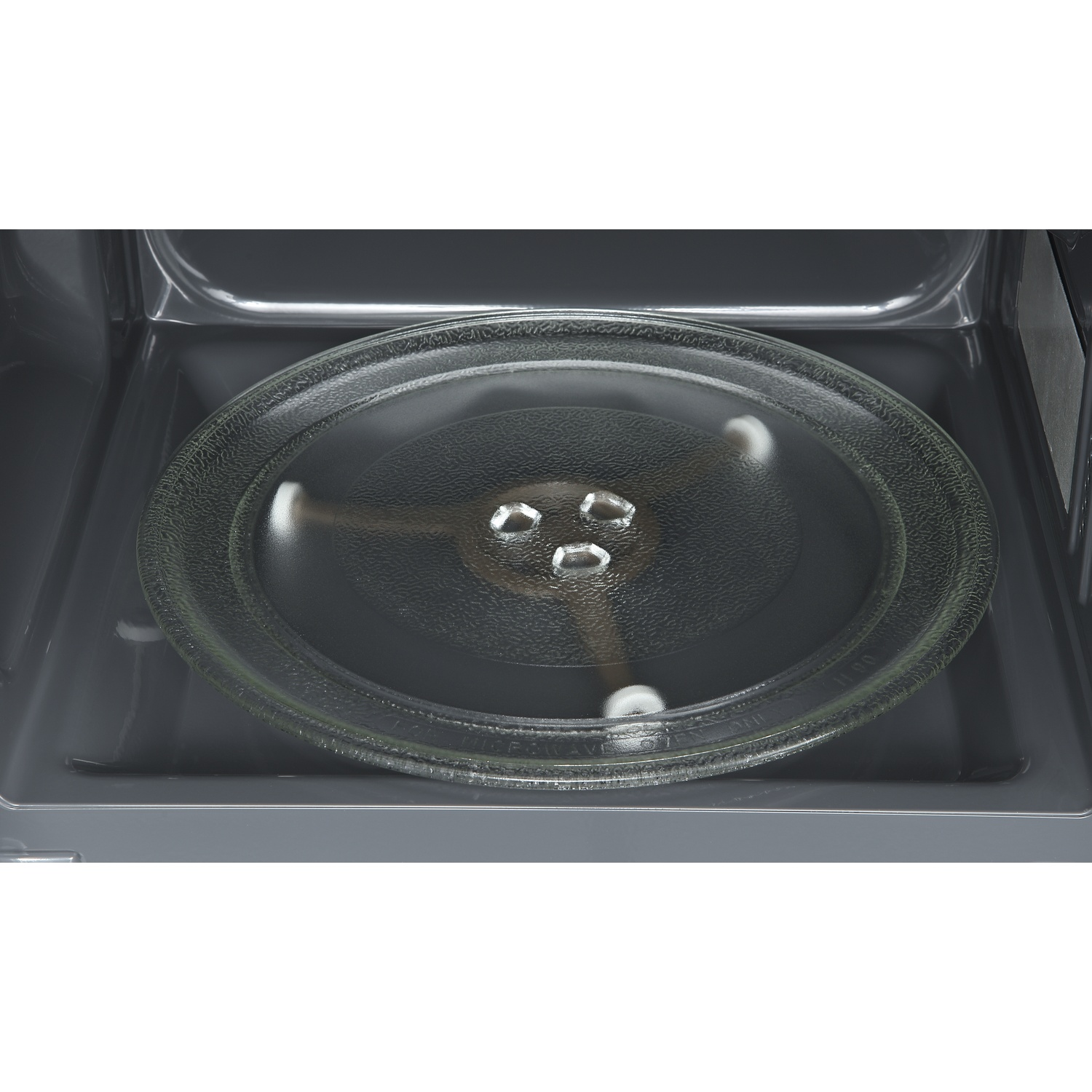 A round glass turntable with three silver supports inside a dark microwave oven.
