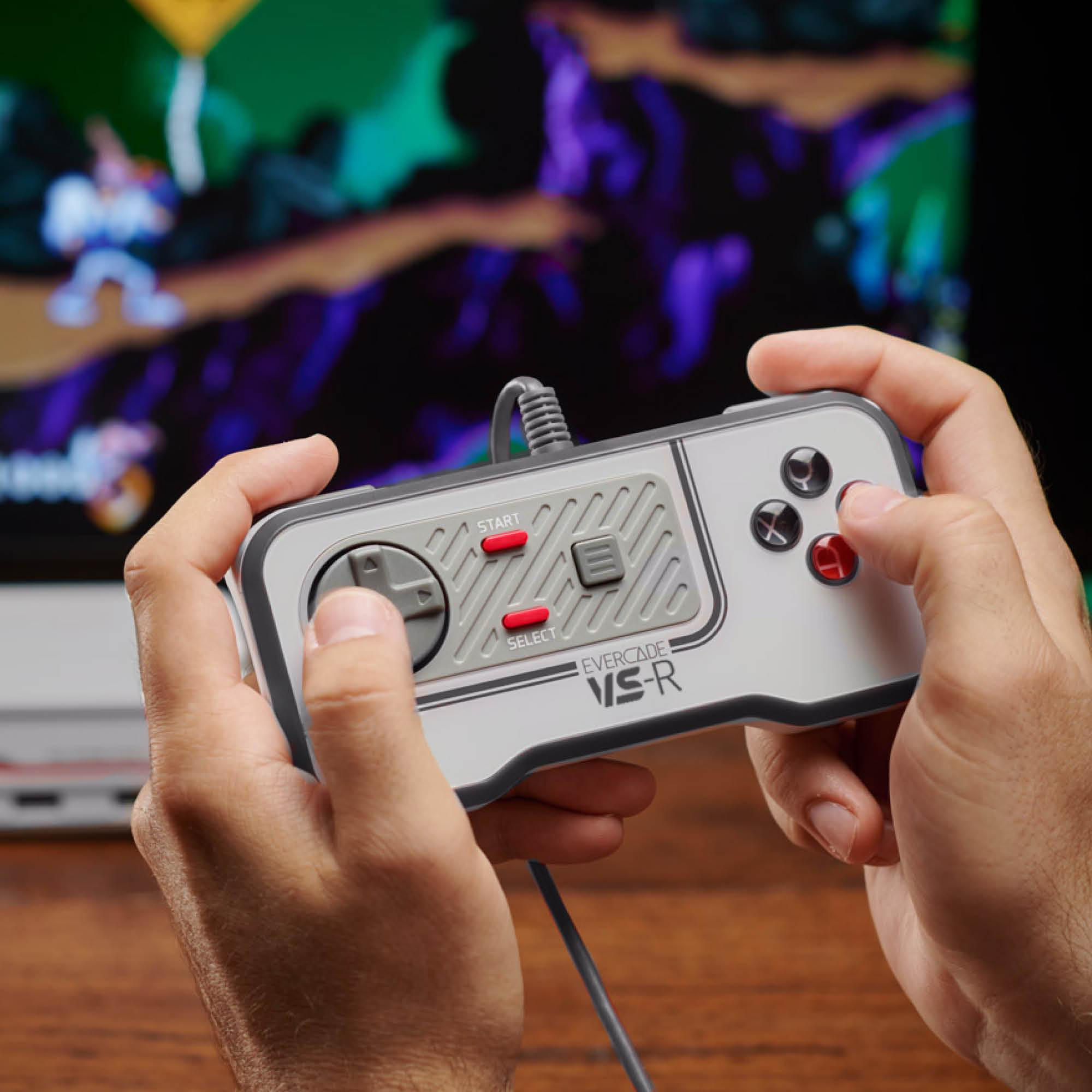 Hände halten einen grauen und weißen Videospiel-Controller vor einem verschwommenen Spielbildschirm.