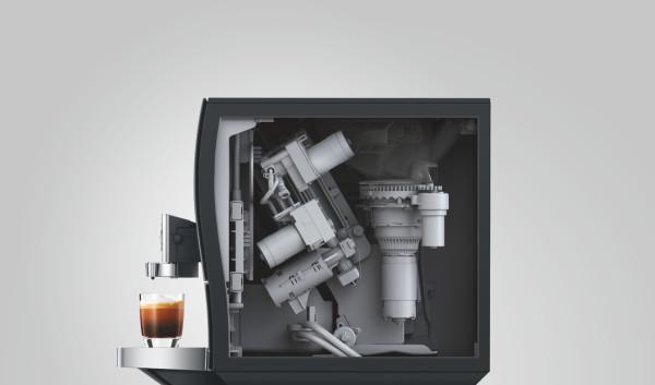 Kaffeemaschine mit freigelegtem Innenleben und einem Glas Espresso daneben.
