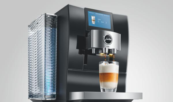 Eine schwarze Kaffeemaschine mit einem Wassertank und einem Glas Kaffee mit Milchschaum.