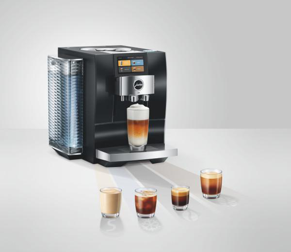 Eine schwarze Jura-Kaffeemaschine macht ein geschichtetes Kaffeegetränk in einem Glas. Drei kleine Kaffeegläser stehen daneben.
