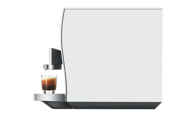 Eine weiße Espressomaschine brüht Kaffee in ein klares Glas auf einer silbernen Abtropfschale.