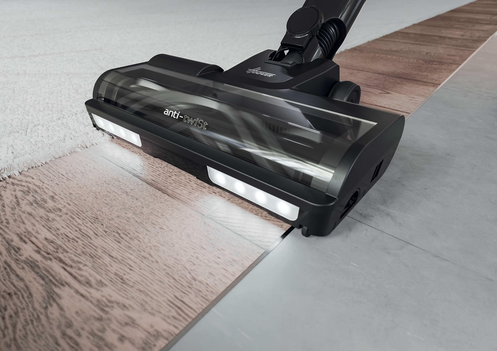 Una testina dell'aspirapolvere nera si muove su pavimenti in legno e moquette.